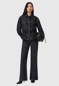 Giacca in denim scuro con due tasche sul petto e vita sfiancata. Pantaloni in denim scuro a gamba larga con una sottile texture macchiata. Accent del borsetta nera.