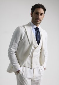 Traje de lino blanco con chaleco de doble botonadura, acompañado de una camisa de vestir azul claro y una corbata azul marino con un patrón sutil.
