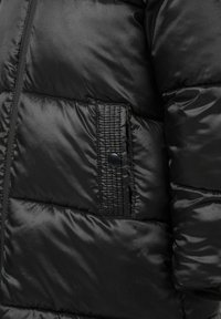 Čierna nafukovacia bunda s hladkou, lesklou textúrou. Obsahuje bočné vrecko so zapínaním na cvok a zúžené švy pre detail.