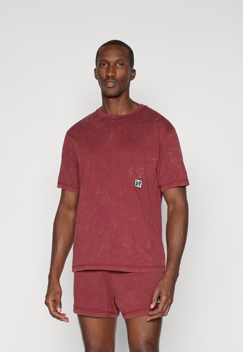 Camiseta de algodón burdeos con cuello redondo y mangas cortas, que presenta un parche de logo cosido en el lado izquierdo del pecho y un corte relajado.