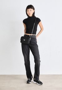 Top corto a righe nere, jeans scuri a vita alta, borsa a tracolla nera con tracolla a catena e sneakers nere; design minimalista e silhouette aderente.