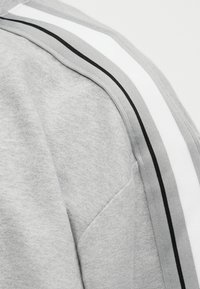 Γκρι ύφασμα με λεπτομέρεια στο ράφι ώμου και επένδυση με παράλληλες ρίγες σε λευκό, ανοιχτό γκρι και μαύρο.