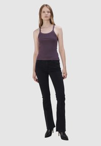 Débardeur violet à côtes associé à un jean noir évasé. Le jean présente un léger effilochage à l'ourlet et est complété par des bottes à talons noires.