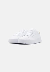 Weiße Leinenschuhe mit runder Spitze, flachen Schnürsenkeln und einer strukturierten Gummisohle. Verfügt über ein dezentes Logo und einen Akzent aus braunem Leder an der Ferse.