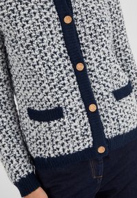 Cardigan lavorato a maglia con un motivo testurizzato bianco e blu navy, con rifiniture blu navy, due tasche frontali e bottoni dorati.