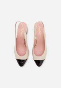 Sapatos slingback bejes com bico fino, apresentando uma ponta em cap toe preta brilhante e palmilha rosa. Feitos de couro liso com um salto baixo.