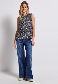 Top senza maniche blu navy con motivo geometrico bianco, abbinato a jeans blu a campana. L'outfit presenta una vestibilità comoda e una texture morbida.