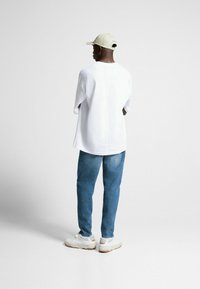 Bílé oversized tričko, světle modré džíny, béžová kšiltovka a bílé tenisky s béžovým akcentem. Jednoduchý design, měkká textura, volný střih.