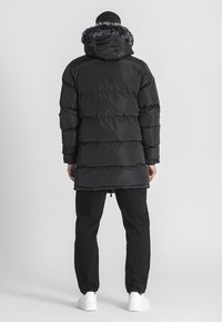 Sort pufferjakke med hætte, der har en faux fur-kant, syede vandrette paneler og et mellemlangt design. Afsat med sorte bukser.
