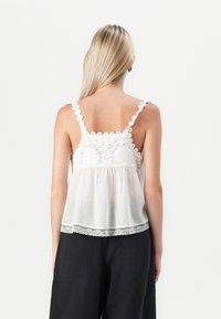 Witte cropped tanktop met bloemenborduursel en kantaccenten, met verstelbare bandjes en een losse pasvorm voor comfort.