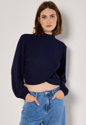 Navy-blau gestreifter, kurzhalsiger Rollkragenpullover mit langen Ärmeln und Wickeldesign, kombiniert mit hellblauen hochgeschnittenen Jeans.