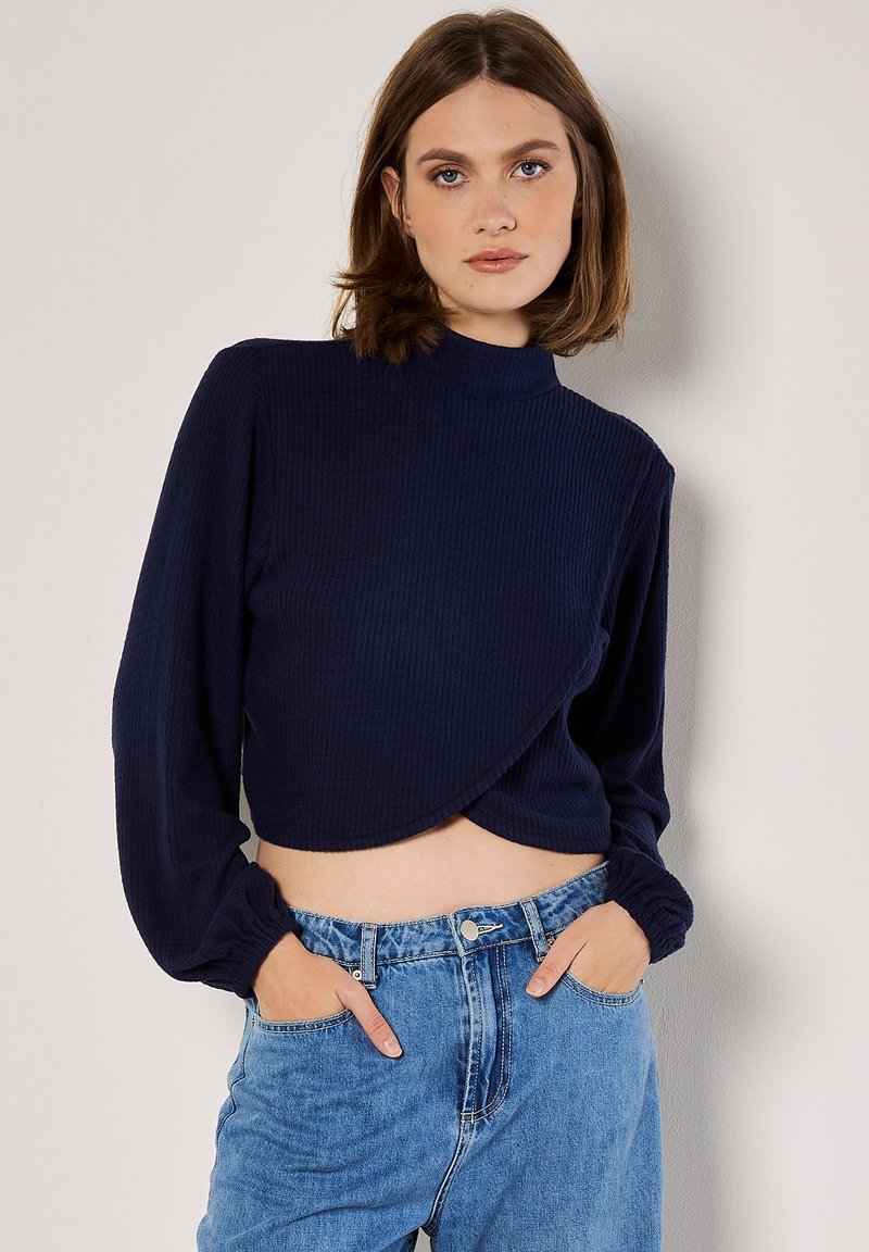 Navy-blau gestreifter, kurzhalsiger Rollkragenpullover mit langen Ärmeln und Wickeldesign, kombiniert mit hellblauen hochgeschnittenen Jeans.