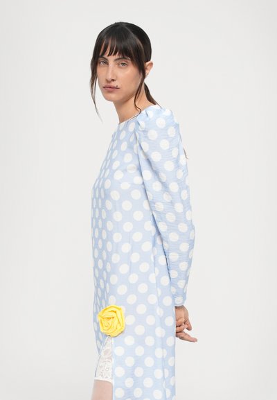 Lyseblå kjole med prikker og pufærmer, med en gul roseaccent på siden og blondekant nederst.