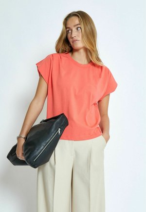 Camisa de algodón coral con mangas cortas y caídas, combinada con pantalones de pierna ancha beige claros y un bolso de cuero negro con cremallera.