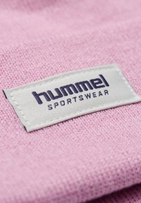 Rosa tyg med en texturerad yta som har en vit etikett med texten "hummel SPORTSWEAR" i mörklila bokstäver.