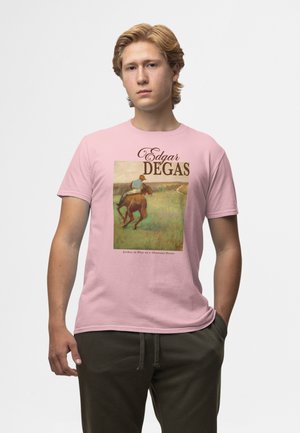 Ung mand med blondt hår iført en lyserød t-shirt med Edgar Degas' maleri "Jockey i blå på en kastanjebrun hest" og mørke bukser.