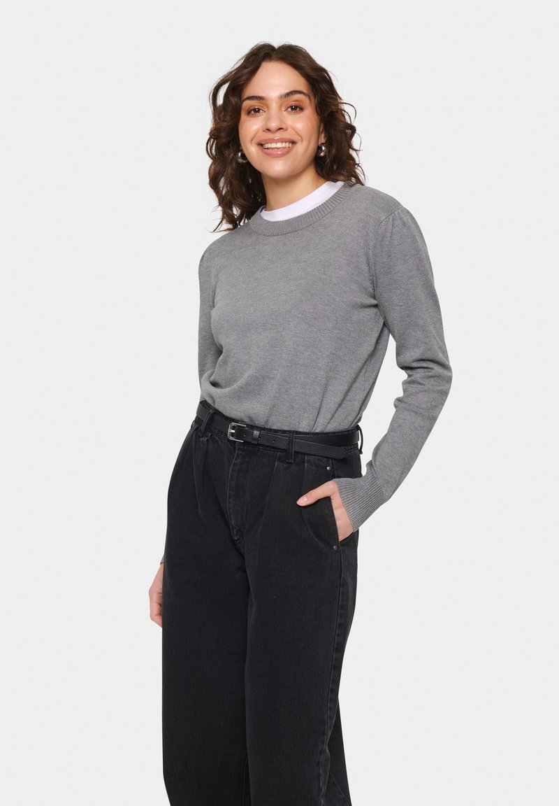Grauer langärmeliger Pullover mit rundem Ausschnitt, getragen mit hochtaillierten schwarzen Jeans, die seitliche Taschen und einen schwarzen strukturierten Gürtel haben.