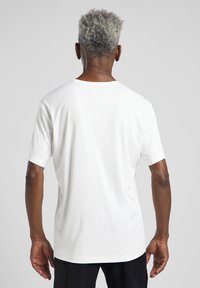 Wit kortom shirt met een relaxte pasvorm, gladde textuur en klassieke ronde hals, gezien vanuit de achterkant tegen een lichte achtergrond.