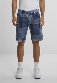 Denim šorti ar plecu dizainu dažādās zilās nokrāsās, ar taisnu griezumu, sarullētām malām un klasisku piecu kabatu stilu.