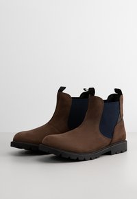 Stivaletti in suede marrone con pannelli laterali elasticizzati blu navy, punta rotonda, altezza caviglia e suole in gomma con motivo di aderenza.