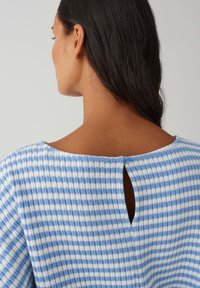 Top a quadri blu e bianco con un'apertura a occhiello sul retro, caratterizzato da un piccolo bottone blu. Tessuto morbido e strutturato.