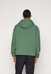 Green hooded jacket with a relaxed fit, featuring a smooth texture and elasticated cuffs, viewed from the back against a white background.
