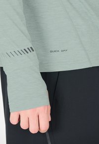 Lichtgroen overhemd met lange mouwen met een "Quick Dry" label. Het heeft een textuur stof en zwarte grafische accenten op de mouw.