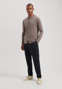 Cămașă gri cu mâneci lungi și nasturi, cu guler, asociată cu pantaloni închiși la culoare și adidași bej. Design simplu cu accente din nasturi.