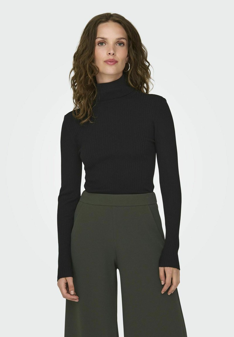 Maglione a collo alto nero a coste con maniche lunghe, indossato con pantaloni a gamba larga verde oliva a vita alta. Texture liscia e design aderente.
