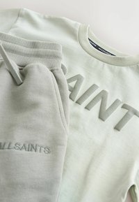 Světlé zelené mikinové tričko s vyraženým nápisem "SAINT" a odpovídající tepláky s žebrovaným pasem, zdobené vyšitým detailem "ALLSAINTS".