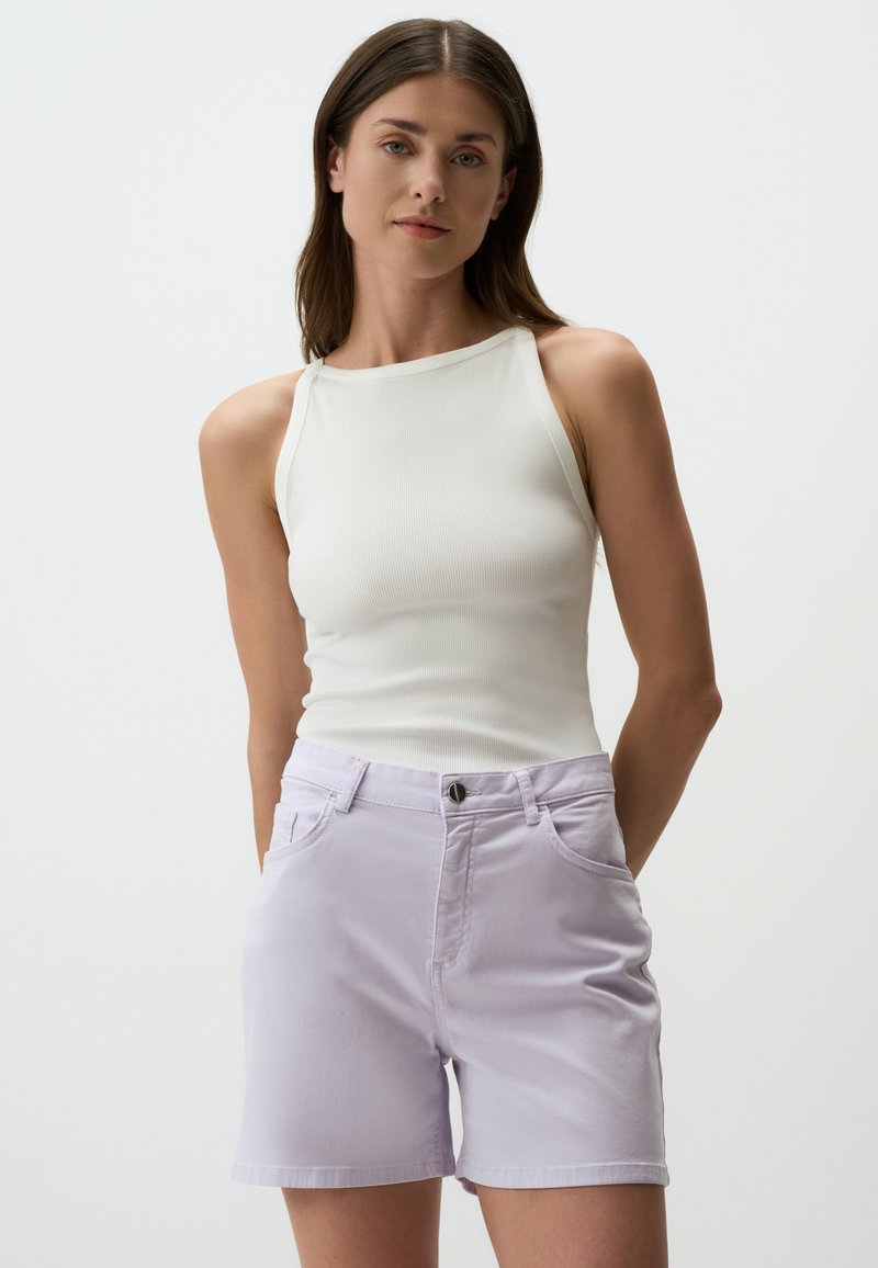 Débardeur blanc à côtes avec un col montant associé à un short en denim lavande clair, comportant des poches avant et une fermeture à bouton noir.