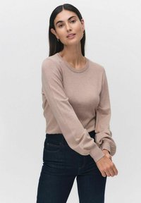 Ljust brunt långärmat tröja med en klassisk rund halsringning, ribbade ärmslut och en mjuk yta, kombinerad med mörka jeans.