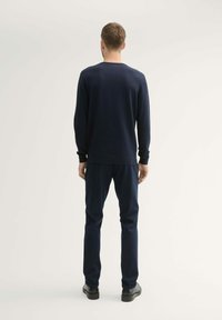 Pull en maille navy à col rond avec des manches longues et des poignets côtelés, associé à un pantalon navy. Texture lisse, design minimaliste.