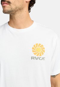 Witte katoenen t-shirt met een gele zonafbeelding en een grijs "RVCA" logo op de linkerkant van de borst. Klassiek ontwerp met een ronde hals.
