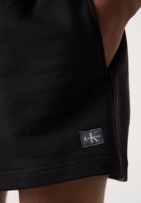 Čierne bavlnené šortky s elastickým pásom a bočnými vreckami, zvýraznené malou obdĺžnikovou nášivkou s logom Calvin Klein.