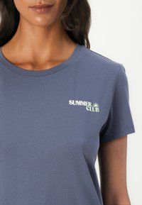 Mørkeblå bomull t-skjorte med korte ermer, med en "SUMMER CLUB"-logo i hvitt og lysegrønt på venstre bryst.