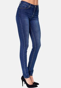 Skinny jeans in dark blue denim with a smooth texture, mid-rise waist, and minimalist front pockets, paired with black high heels.