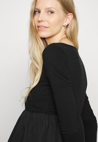 Blusa preta de mangas longas com corpo justo e saia rodada. Textura suave, decote redondo e detalhe de cintura elástica.