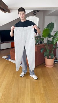 Pantalones de chándal grises hechos de una tela suave, con una cinturilla elástica y cordones, además de bolsillos laterales, exhibidos por una persona en el interior.