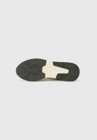 Semelle en caoutchouc noir avec un motif texturé et des accents crème. Présente un design bicolore et des détails moulés pour une meilleure adhérence et un soutien optimal.