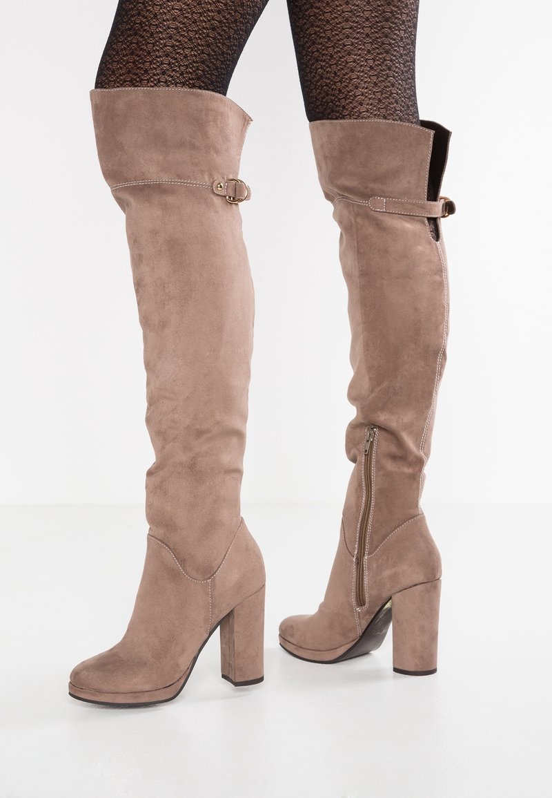 Botas de ante hasta el muslo en tono topo, con un tacón bloque, cremallera lateral y un hebilla decorativa en la parte superior. Textura suave y diseño ajustado.