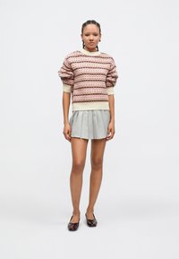 Suéter de punto con franjas horizontales en rosa y crema, mangas abullonadas, combinado con una falda plisada gris y zapatos planos oscuros brillantes.