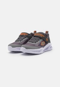 Zapatos deportivos grises con acentos naranjas, parte superior de malla, collar acolchado y suela de goma blanca con un diseño texturizado para tracción.