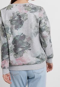 Sudadera gris con un estampado floral en tonos verdes y rosas. Puños y dobladillo acanalados que aportan estructura. Tejido suave y texturizado.