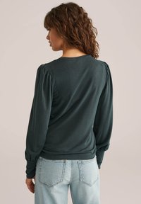 Sötétzöld, hosszú ujjú blúz puffadt vállakkal, puha anyagból készült, kerek nyakkivágással és szabott siluettel. Kényelmes megjelenés.