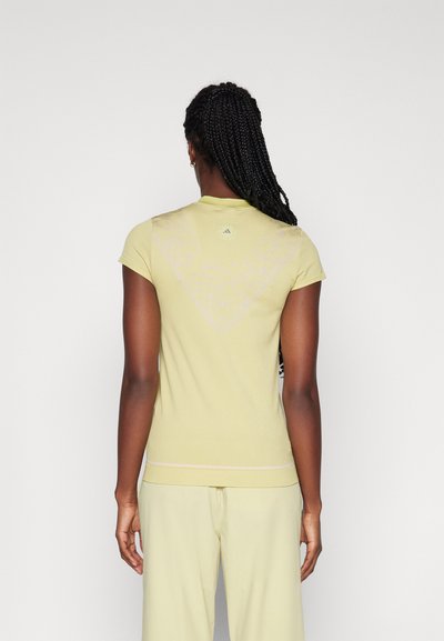 Chemise jaune clair à manches courtes avec un col arrondi, présentant un design triangulaire à motifs au dos et un détail discret à l'ourlet.