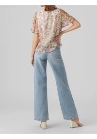 Haut blouson transparent à motif floral avec manches courtes, associé à un jean large bleu clair et des sandales beige à talons blocs.