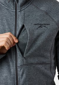 Grijze zip-up jack met een gestructureerd patroon, zijzak met ritssluiting en logo op de borst. Hoge kraag en slim fit ontwerp.