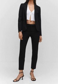 Blazer negro entallado sobre un top corto blanco, combinado con pantalones negros ajustados y tacones negros con tiras. Tejido suave con líneas limpias.
