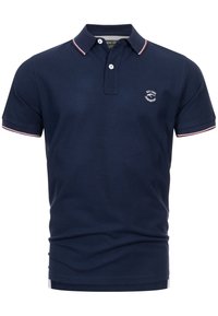 Polo shirt bleu marine en coton lisse, avec une patte de boutonnage à deux boutons, un col et des bords de manches rayés blanc et rouge, et un logo sur la poitrine.
